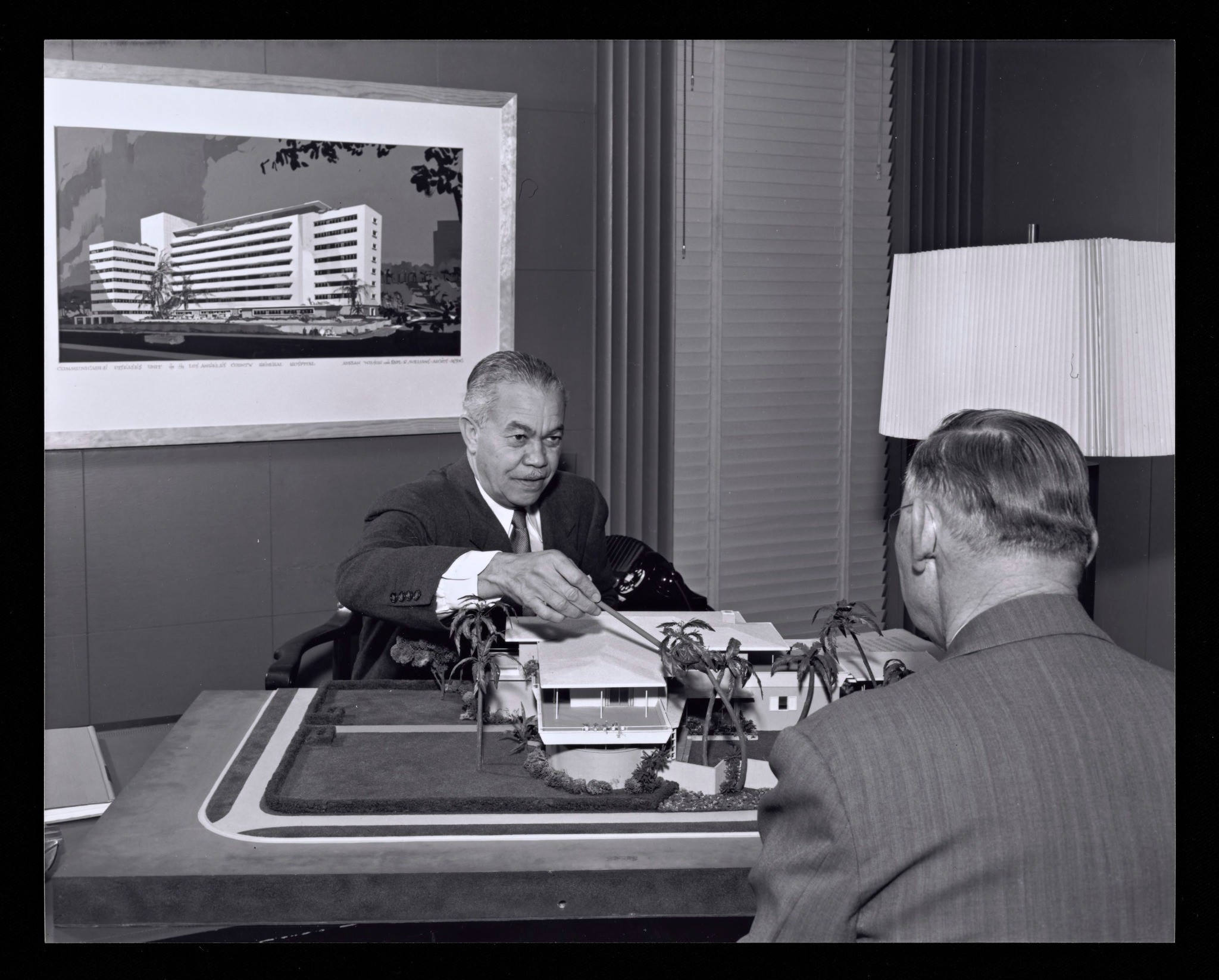 Paul R. Williams seated at his office desk in conversation with a visitor.